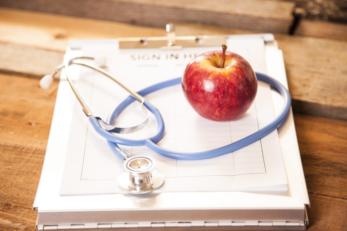 apple and stethoscope on top of a clipboard