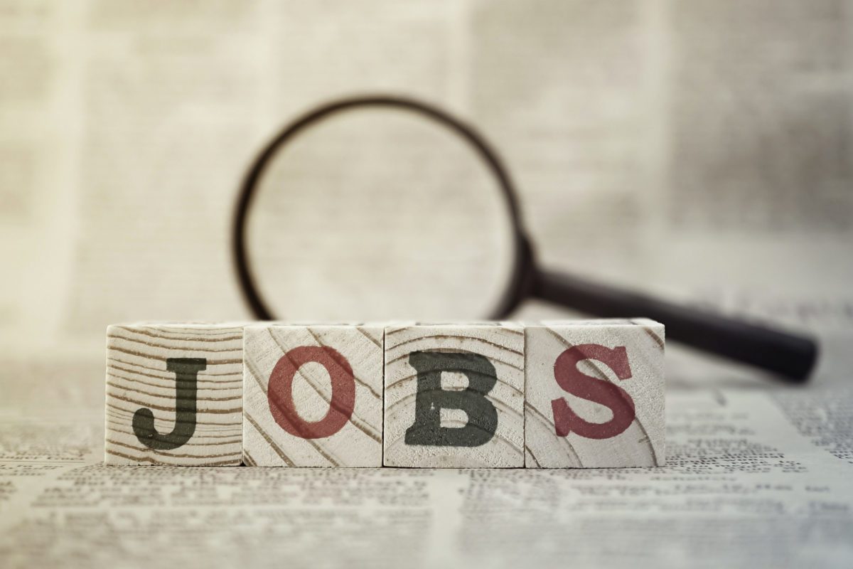 "Jobs" on wooden block and magnifying glass on newspaper background