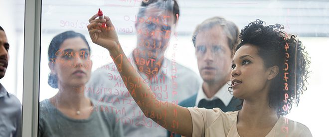 woman writes on a glass board during a brainstorming meeting