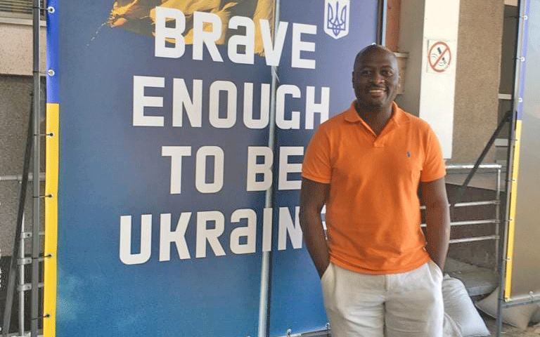 Sammy K. Ngichabe standing in front of a sign that says, "Brave enough to be Ukraine"