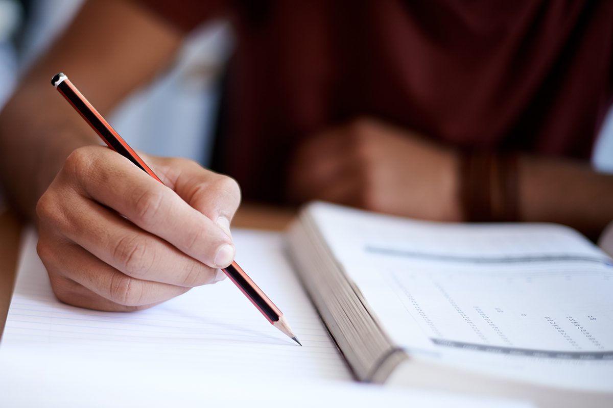 Closeup shot of a young person wearing a red shirt writing on a note pad