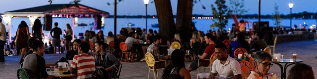 A shot of the terrace at night, full of people sitting at tables and by the docks, eating and drinking
