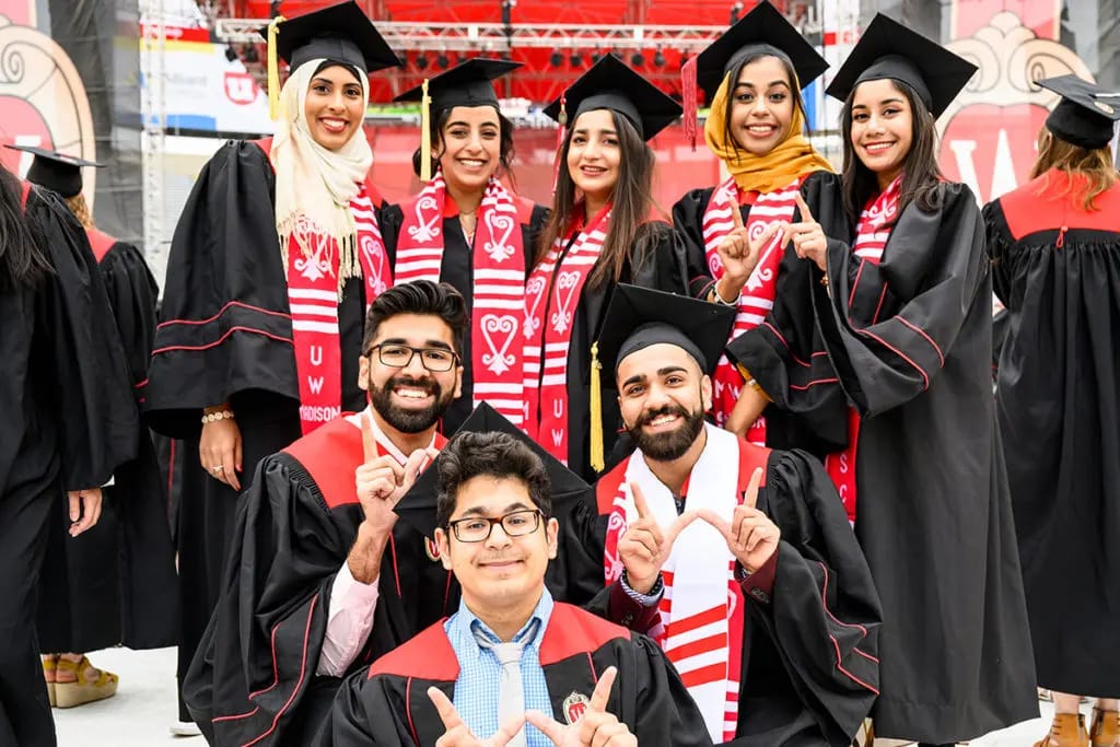 UW-Madison graduates in their cap and gowns posing for a group selfie.