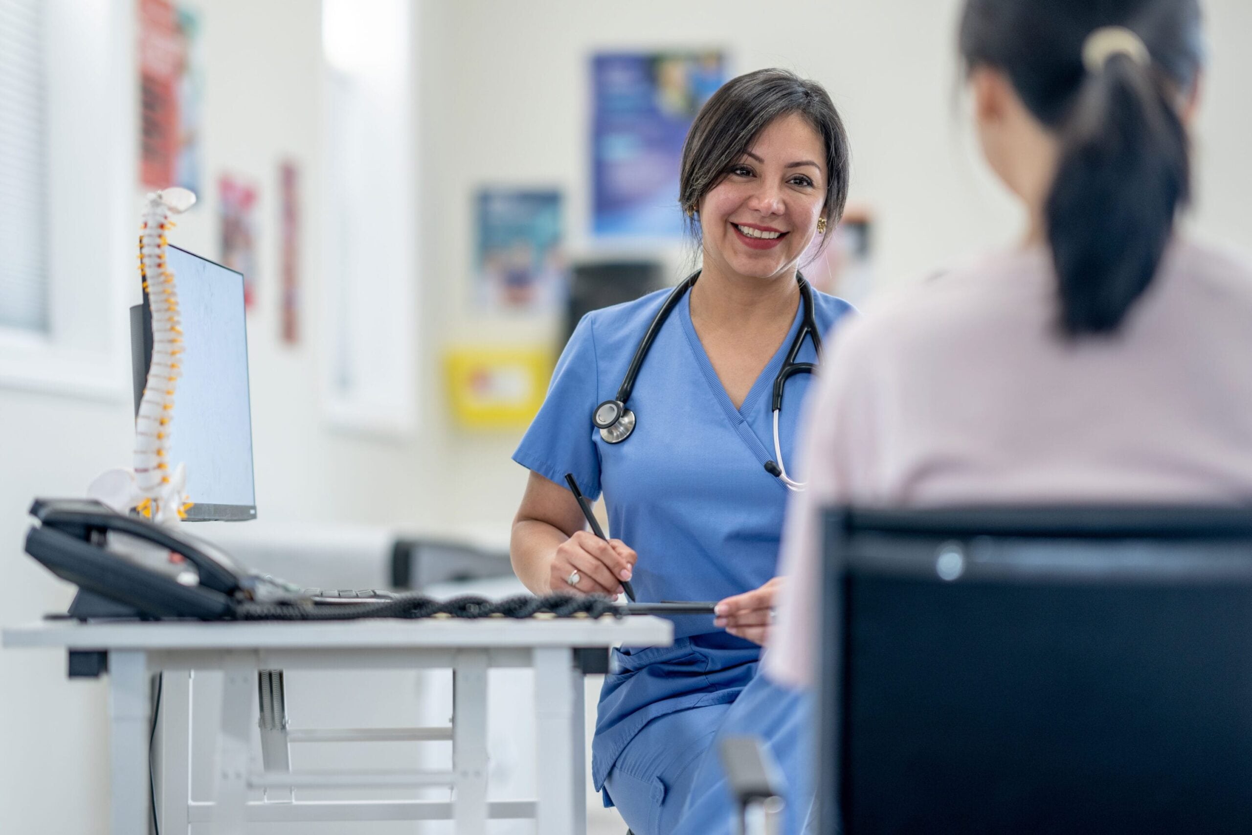 A patient sits on a metal chair as she speaks with a nurse.