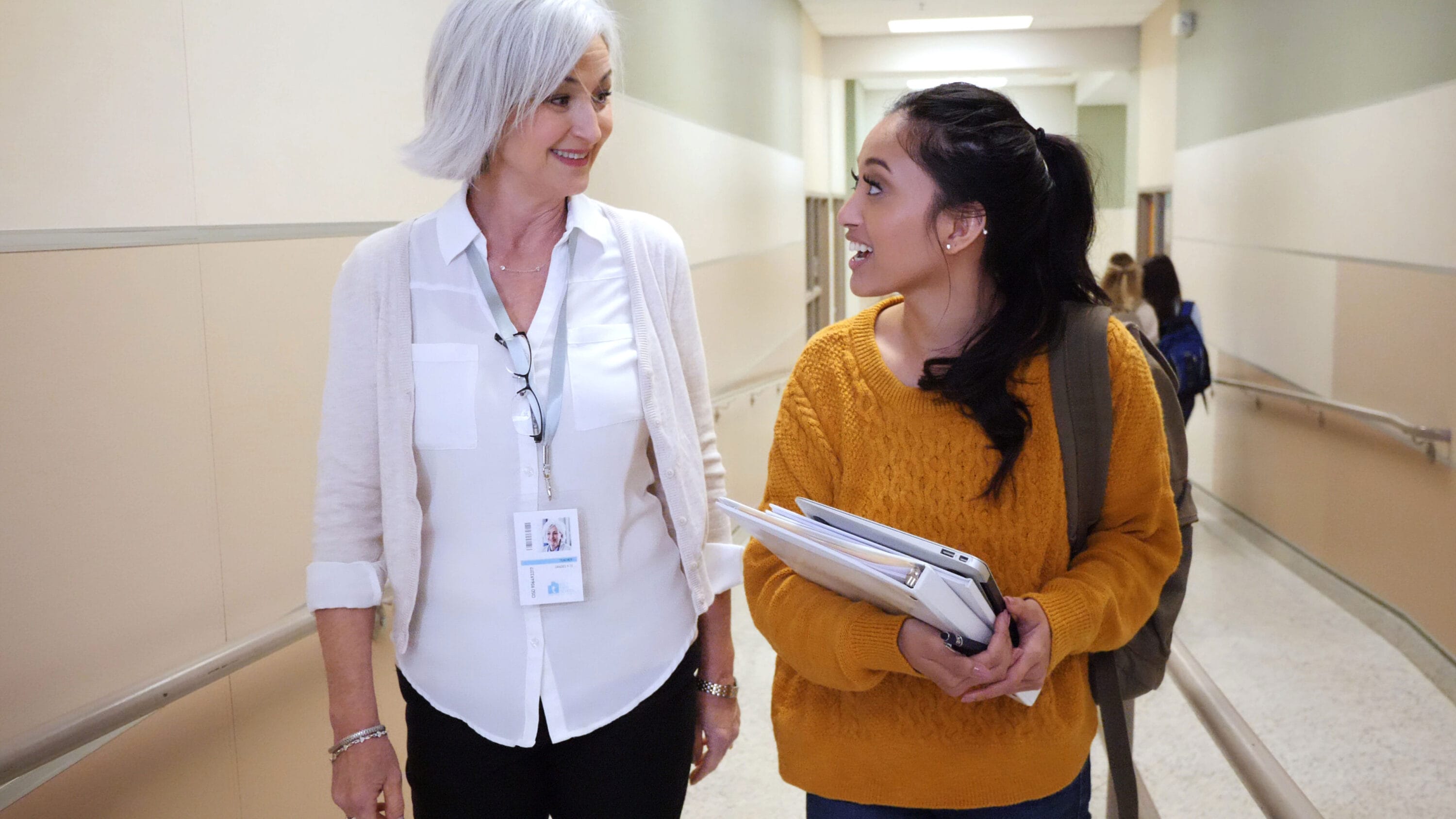An older woman and a younger woman are walking down a hall having a conversation.