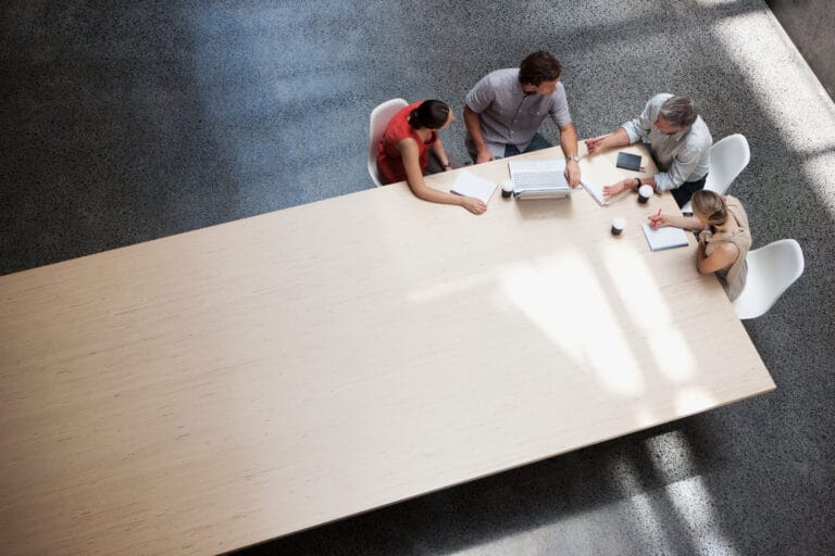 An aerial view of four people reviewing documents around a conference table.