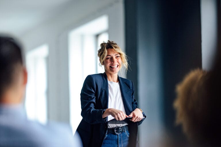 A woman in casual business attire smiling at a group of people.