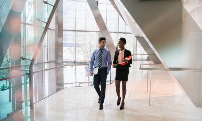 A man and a woman dressed in business attire walking down the hallway of an office building