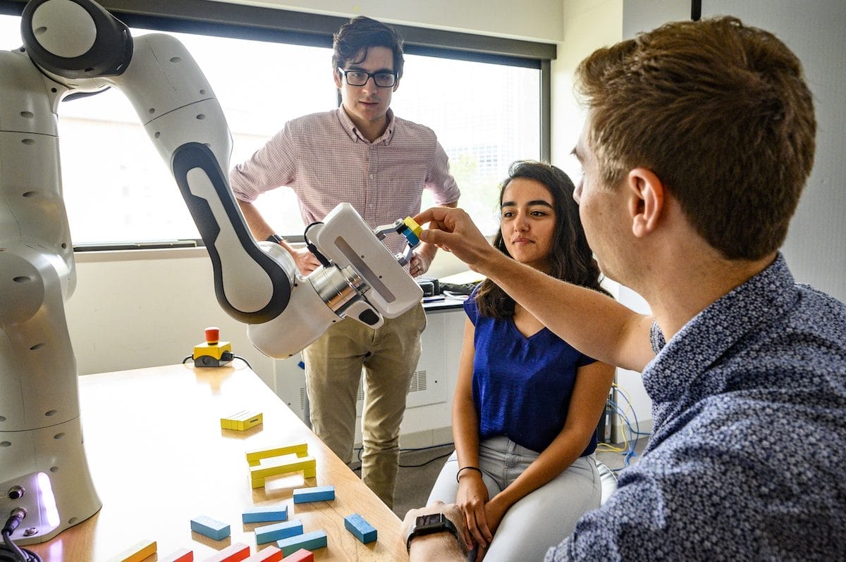 Three engineering students playing with a mechanical arm