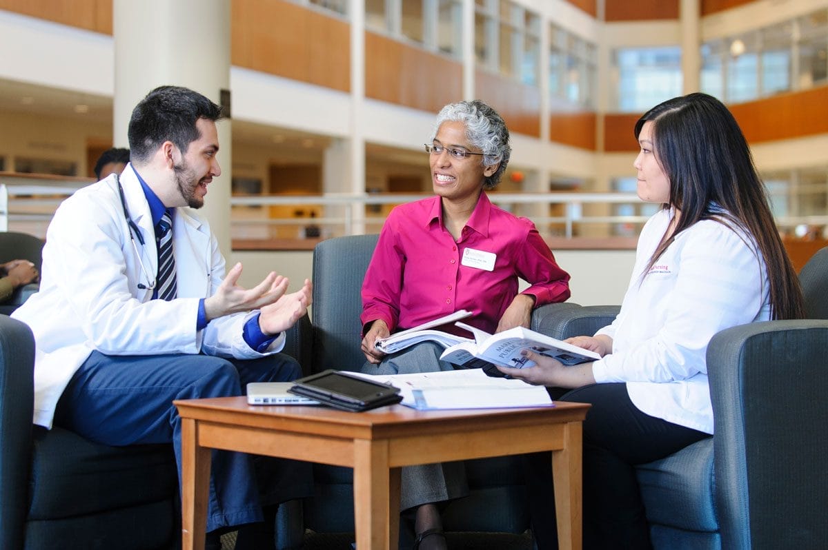 Two nursing students sitting down with a doctor to hold a conversation