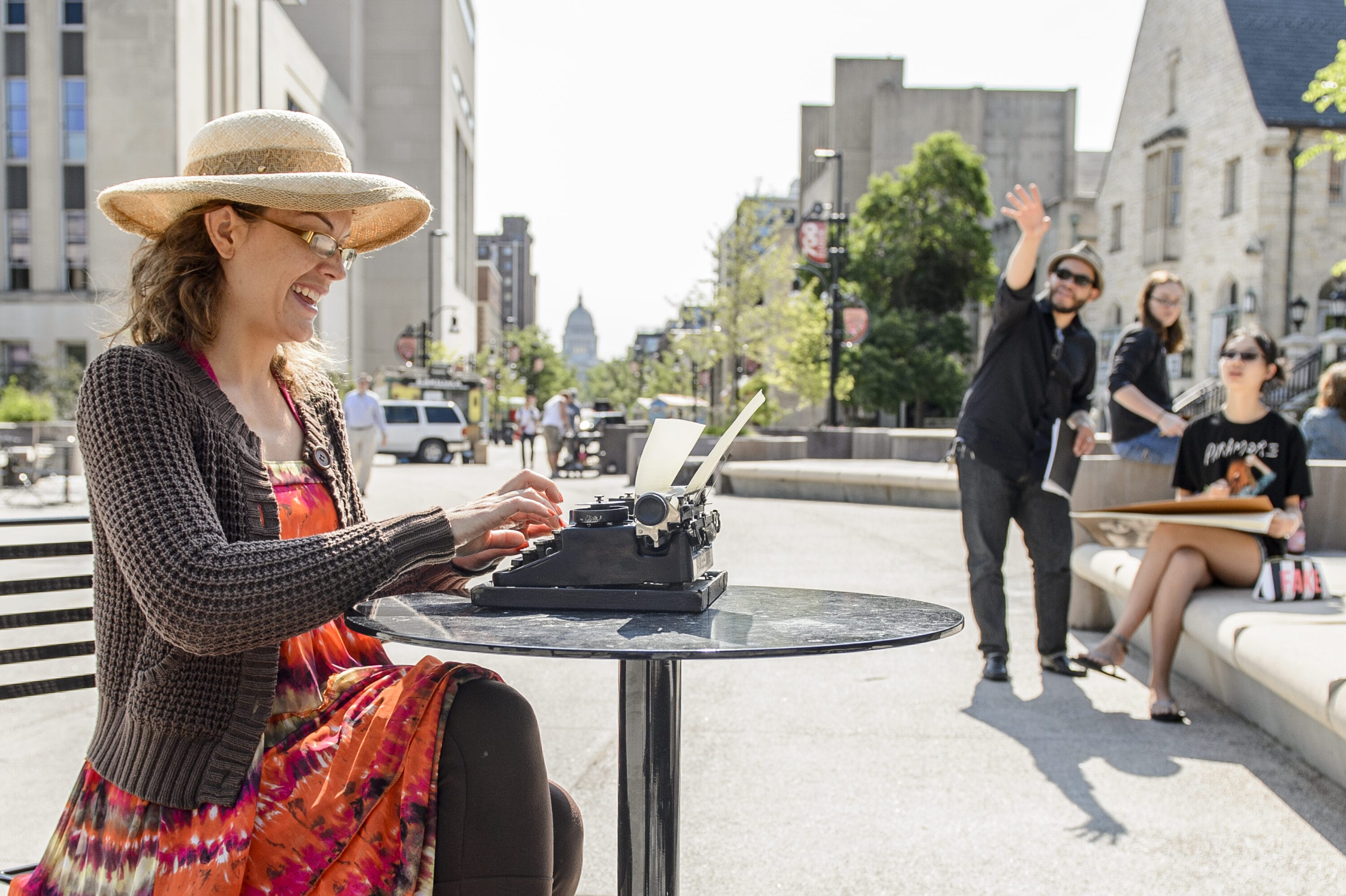 A woman sitting at a table in the Library Mall typing on a typewriter.