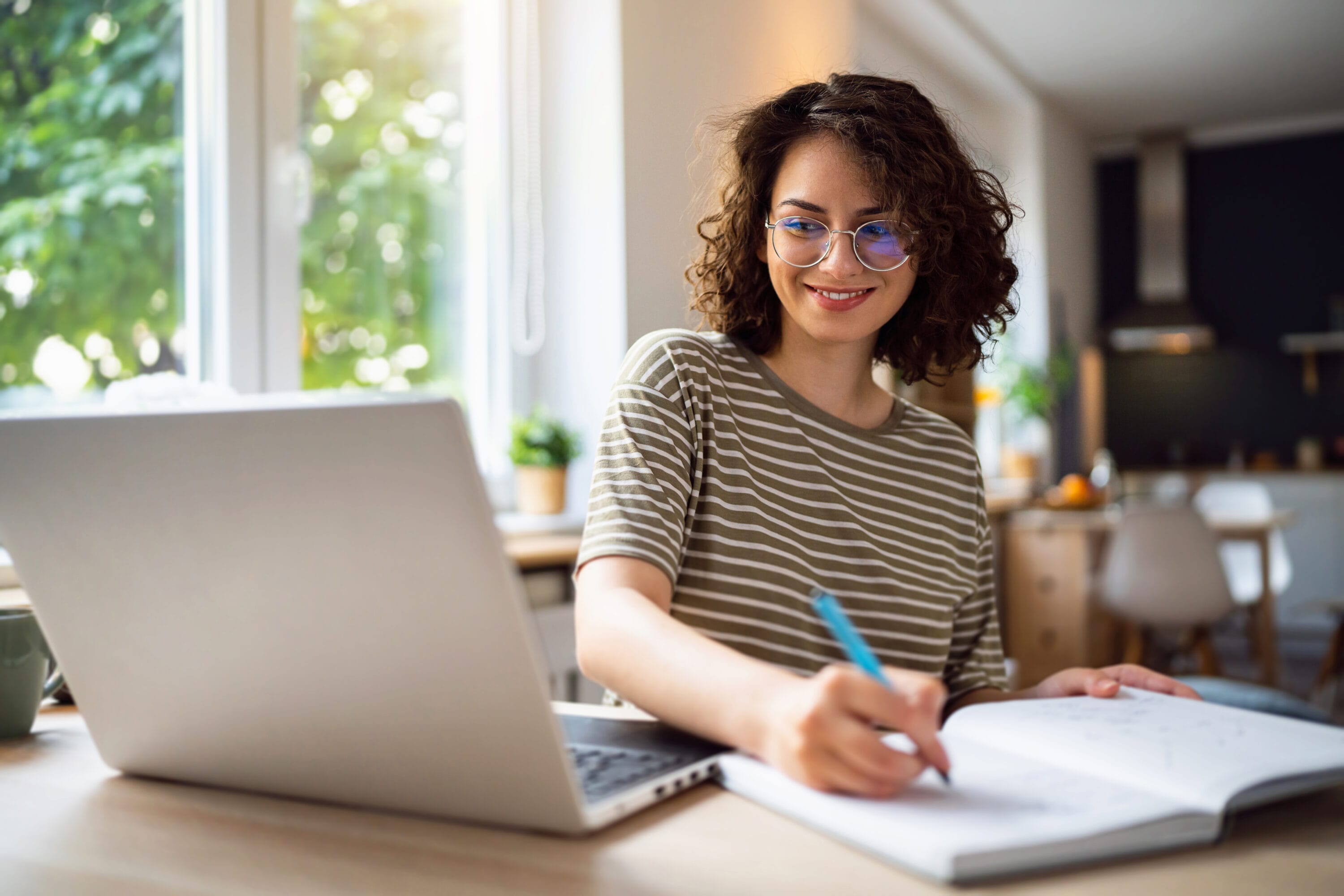 A woman reading something on her laptop and jotting down notes on a notebook.