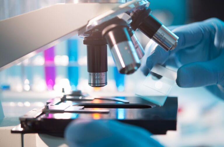 A closeup of a pair of gloved hands slipping a specimen under a microscope