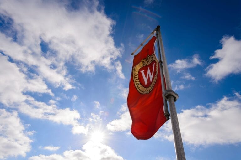 A shot of a flag of the UW-Madison crest billowing in the wind on a sunny day