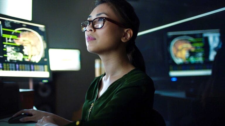A woman in a dark room surrounded by many computer screens