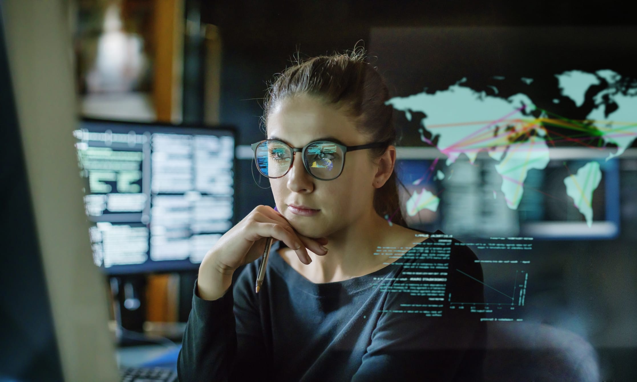 A woman wearing glass reviewing a series of numbers on a computer monitor