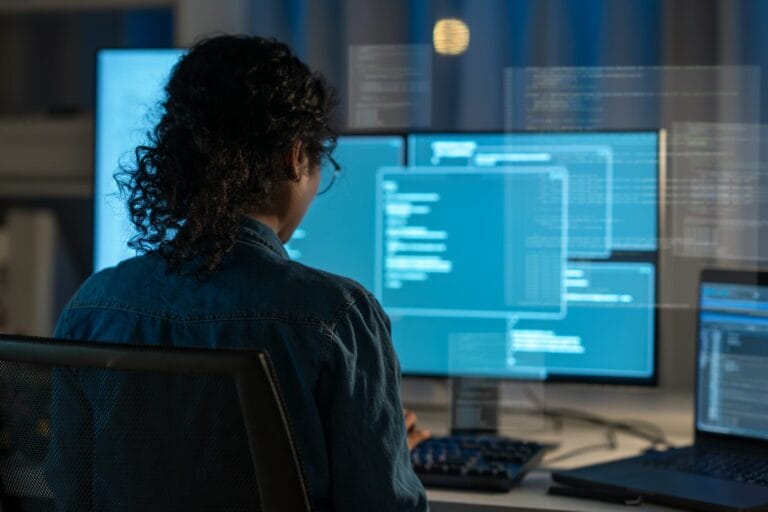 A woman writes code on a computer with multiple screens