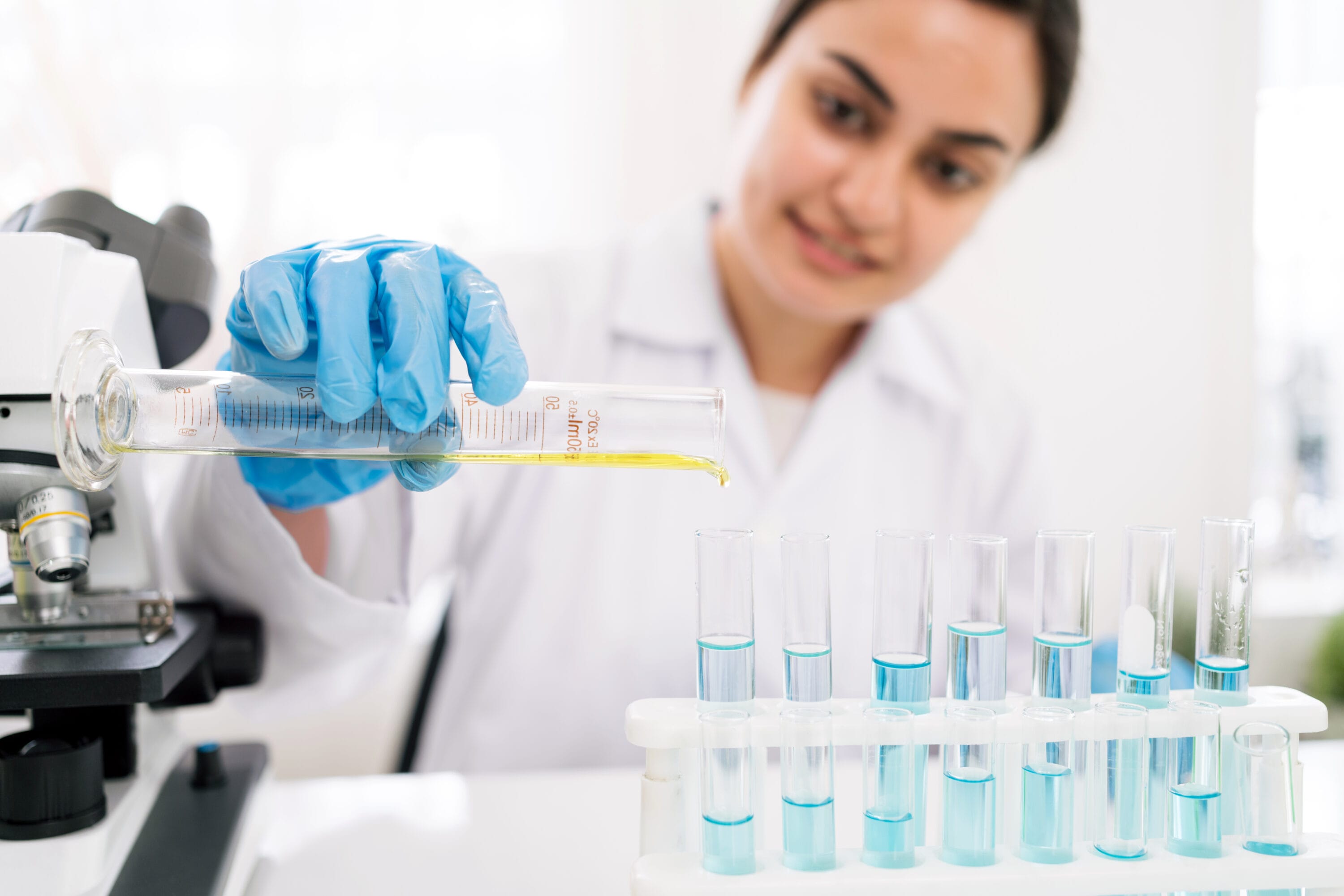 A woman in a lab coat pouring a yellow substance in a test tube.