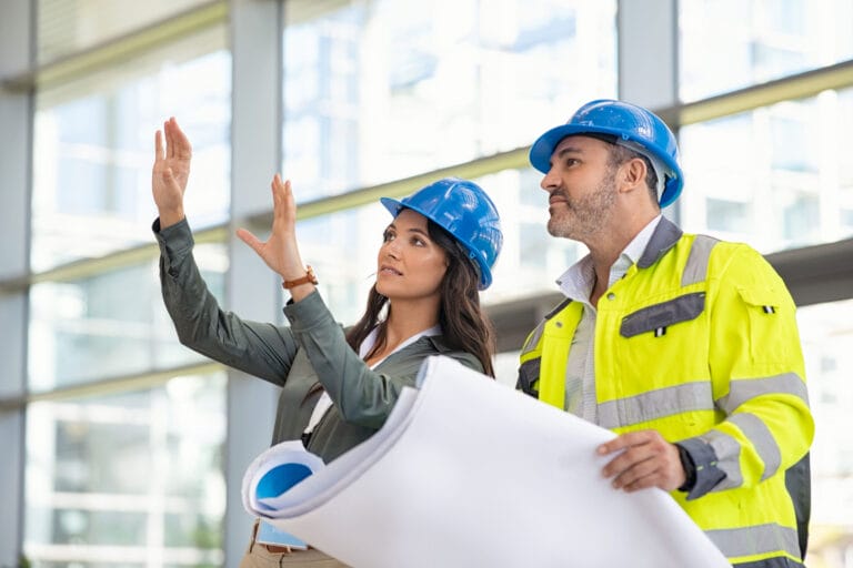 A man and a woman wearing hardhats on a construction site, visualizing a build.