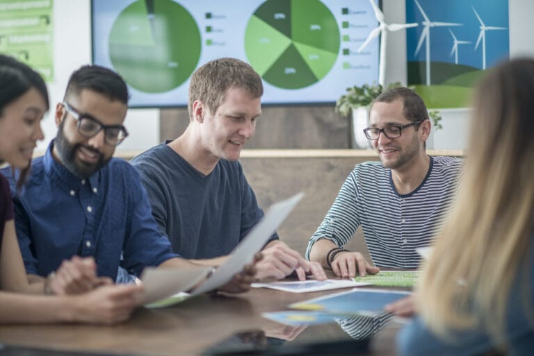 A group of professionals holding a meeting with graphical documents in the background.