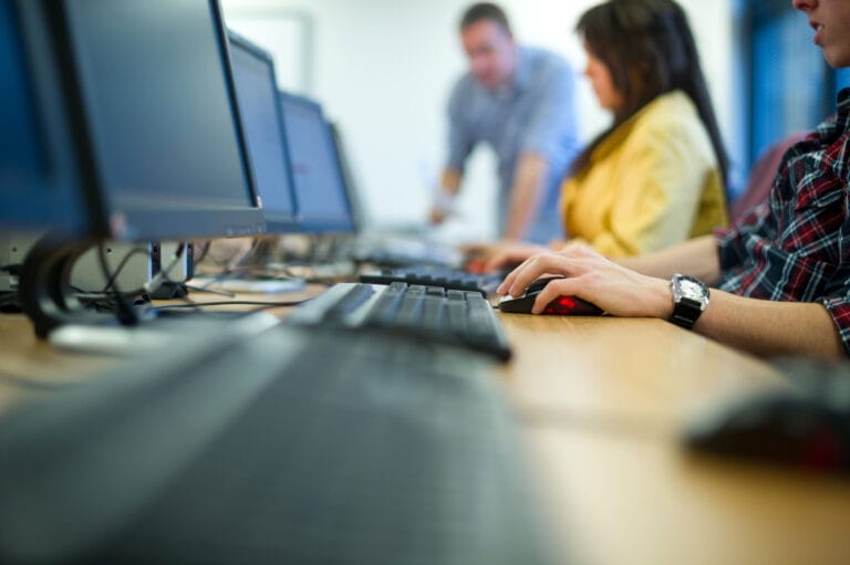 Three people typing on a keyboard in a computer room.