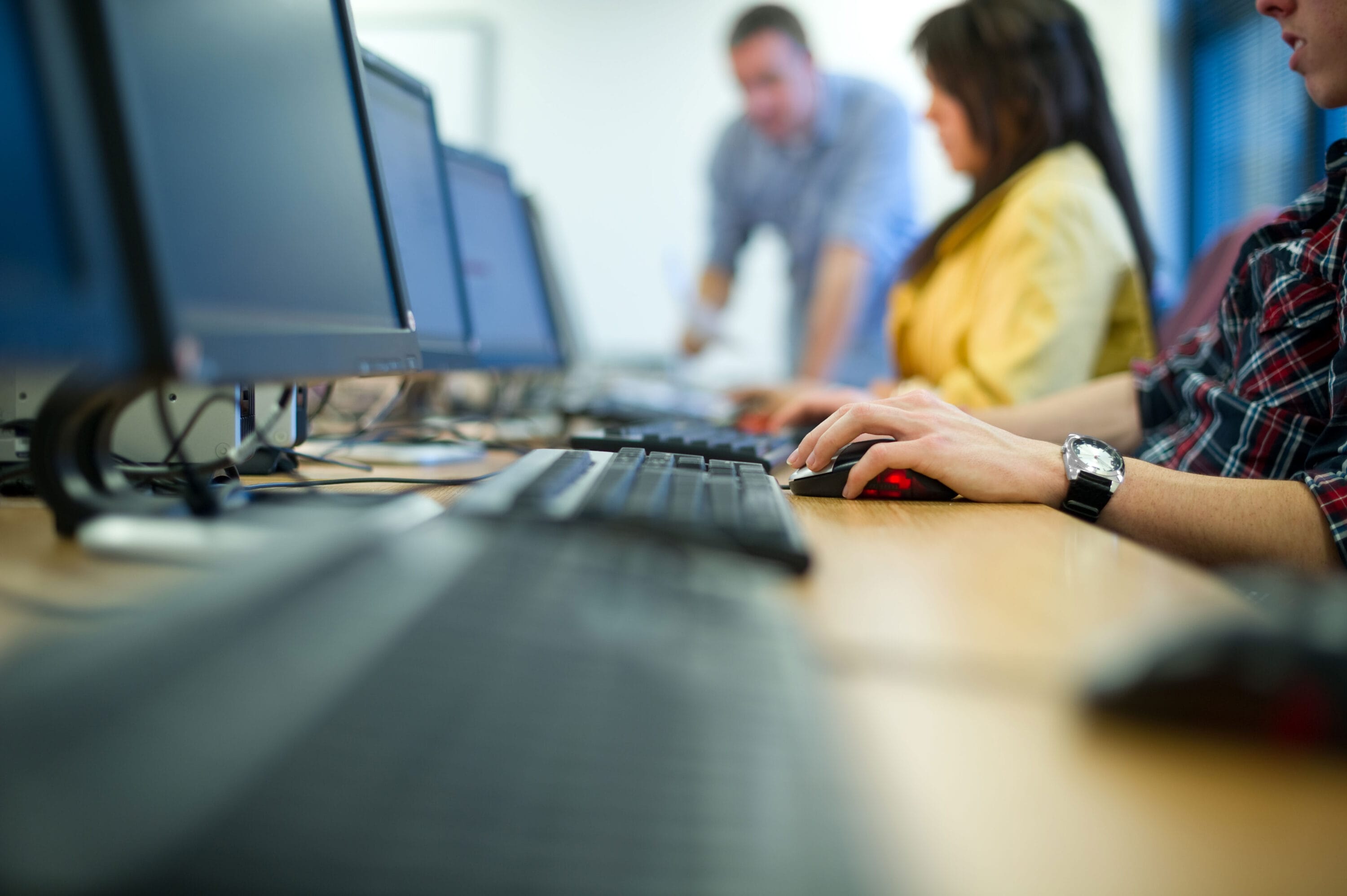 Three people typing on a keyboard in a computer room.