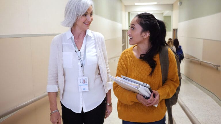 An older woman and a younger woman are walking down a hall having a conversation.