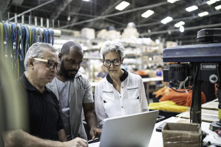 Three workers huddled around a laptop in a warehouse.