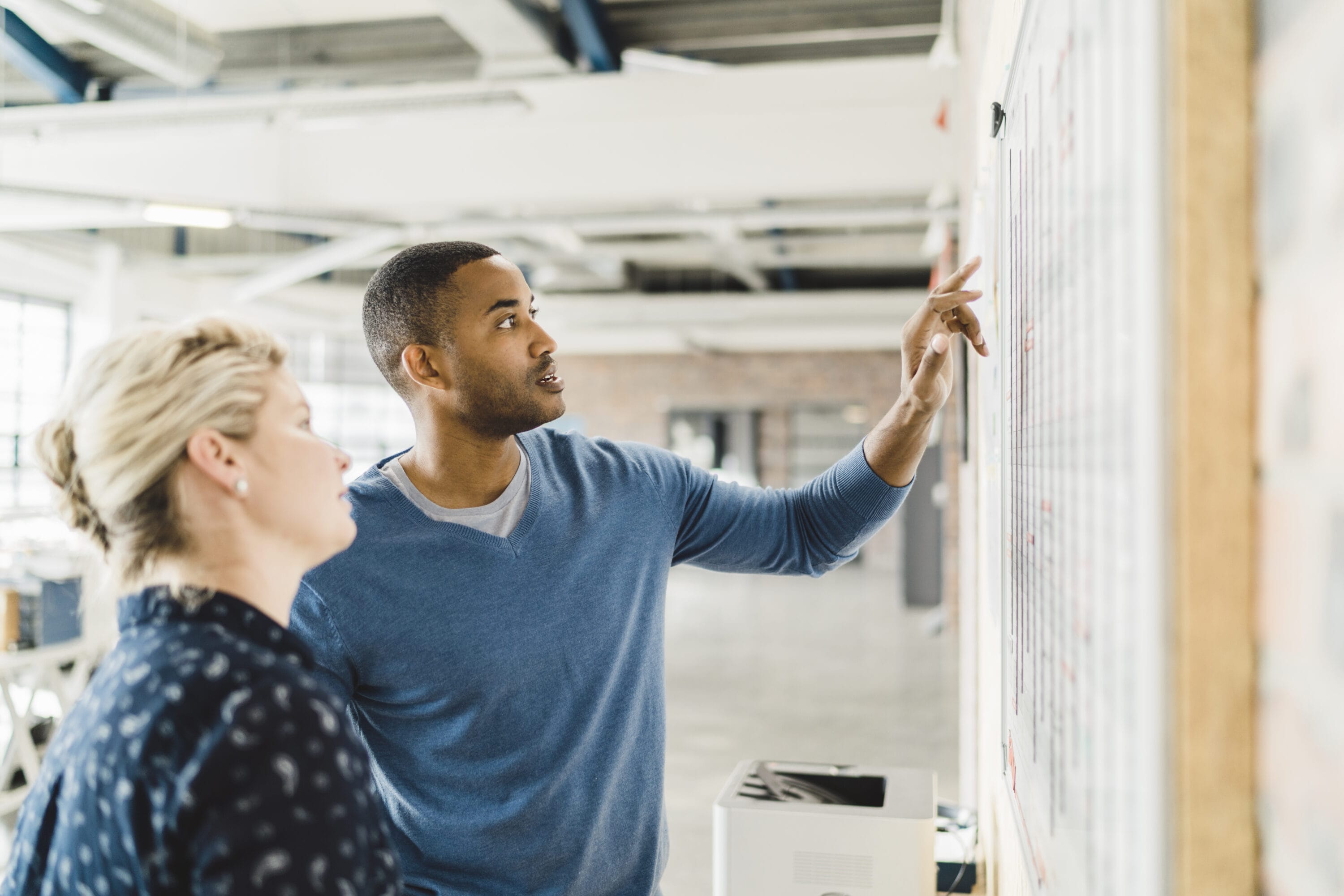 A man and a woman in a classroom are reviewing plans on a whiteboard.