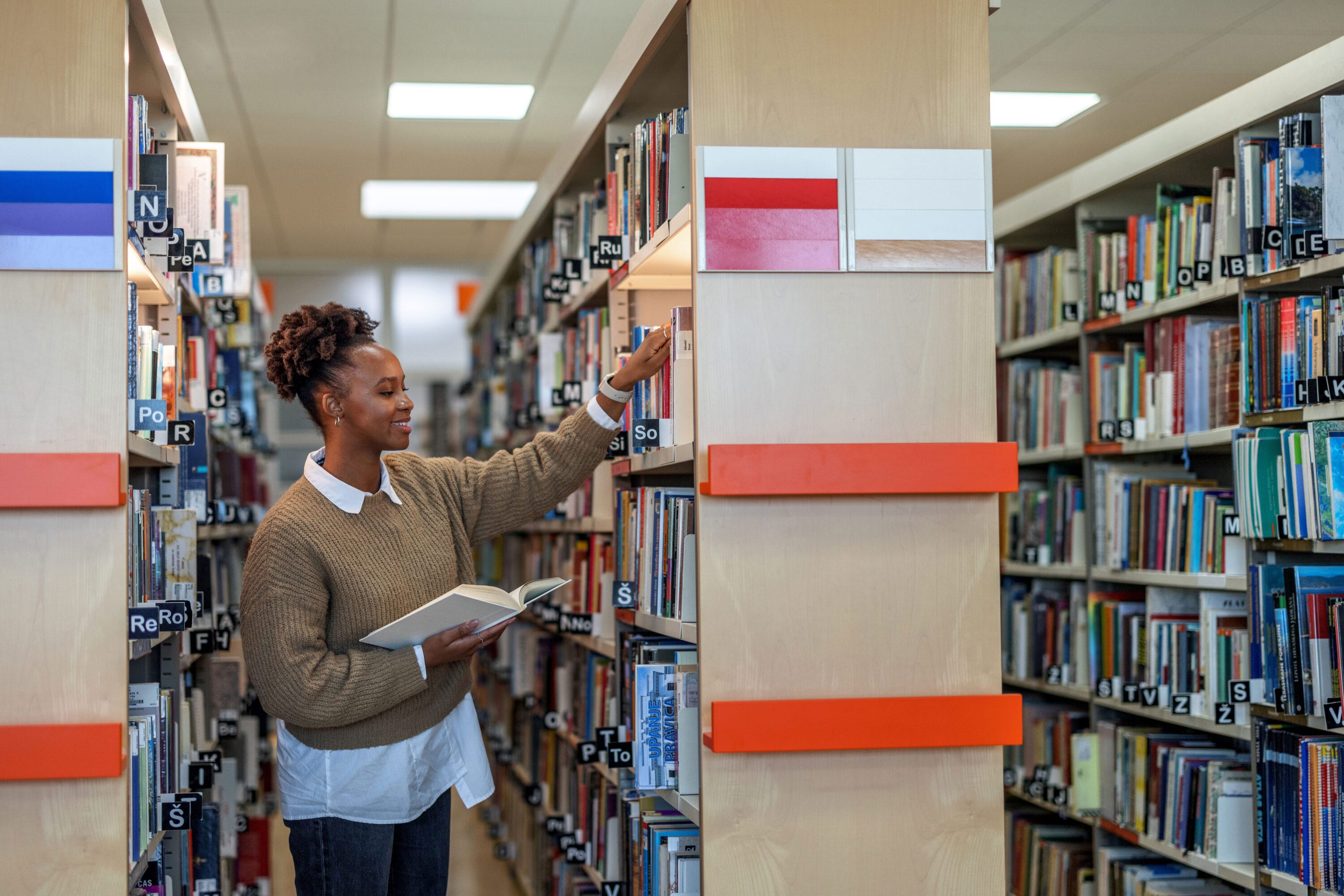 A woman in a library pulling a book from the shelf.