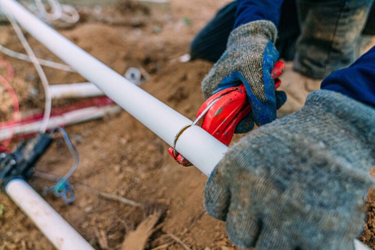 A construction worker cutting into a white pipe.