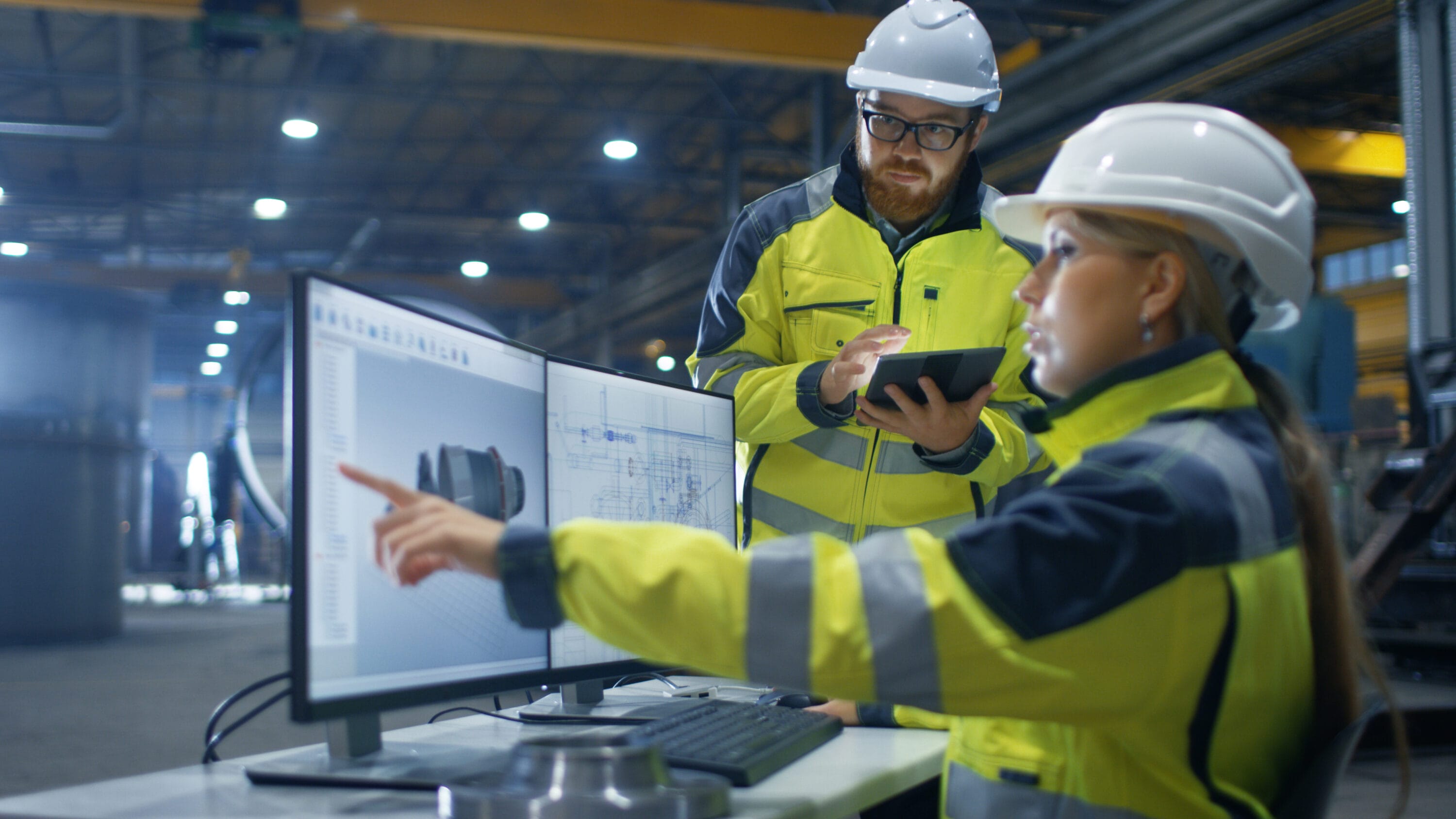 Two engineers wearing protective gear reviewing data on a computer monitor.