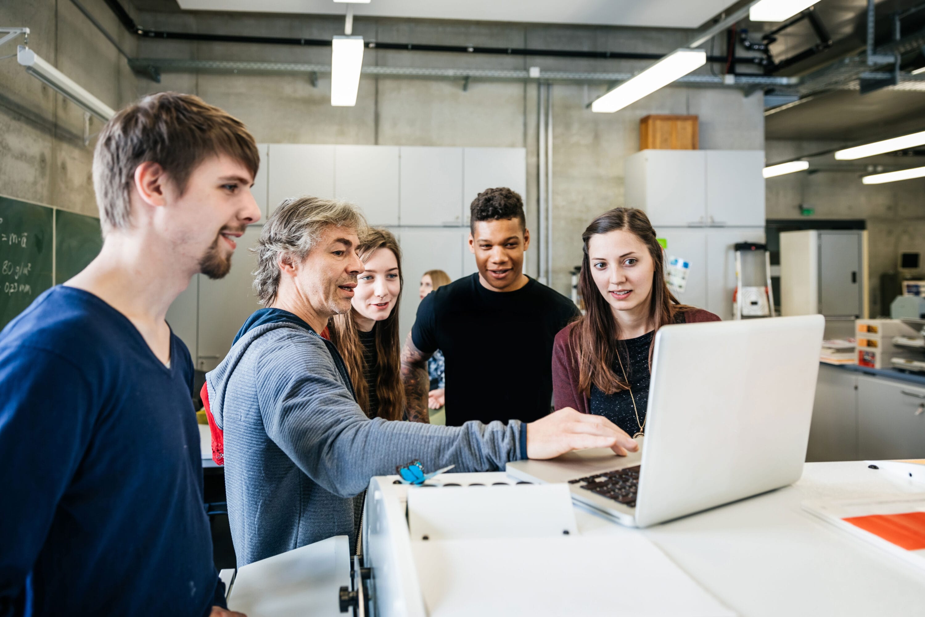 A group of engineers meeting and discussing a plan around a laptop.