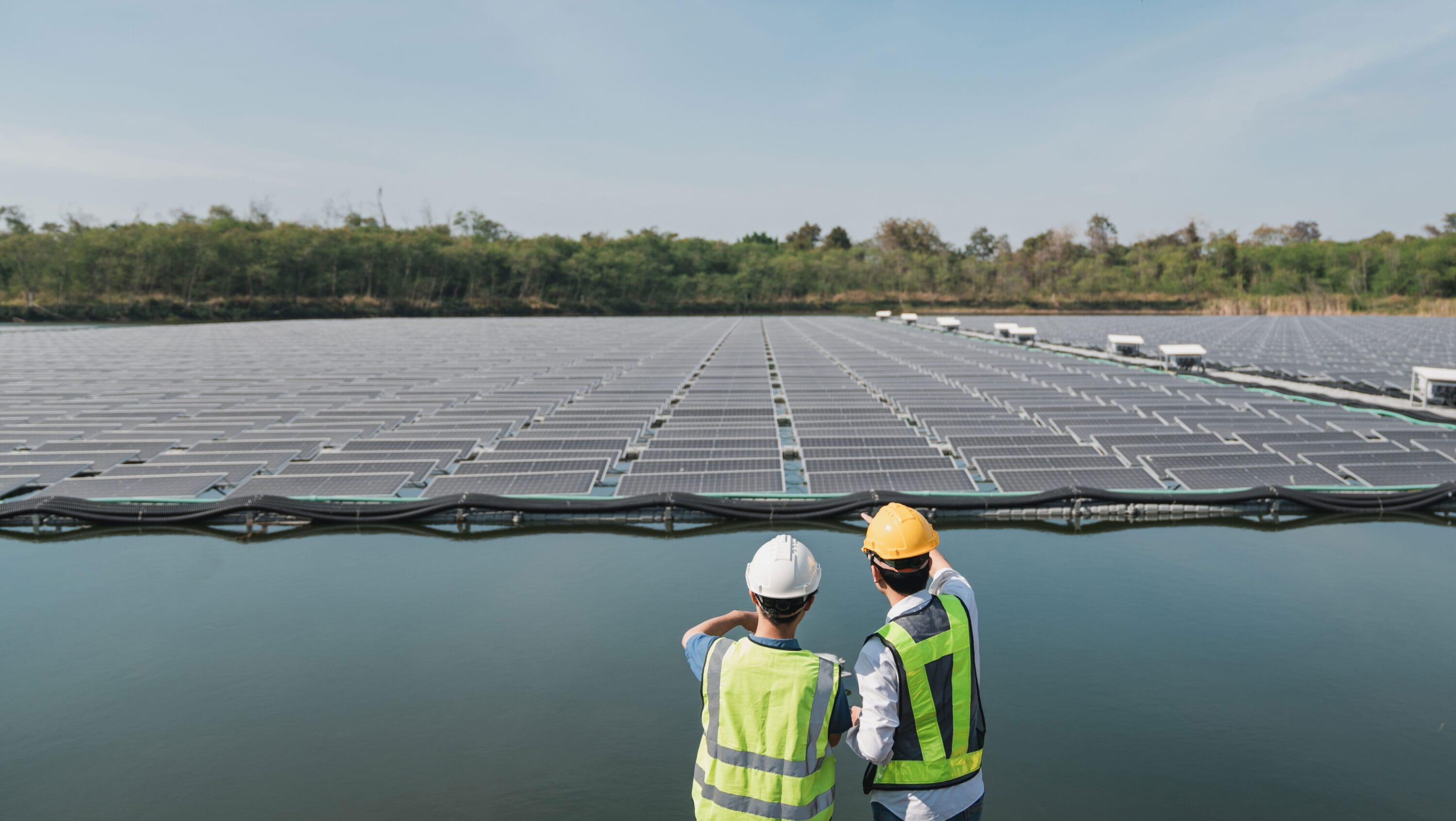 Two workers in protective gear standing before a solar panel field.