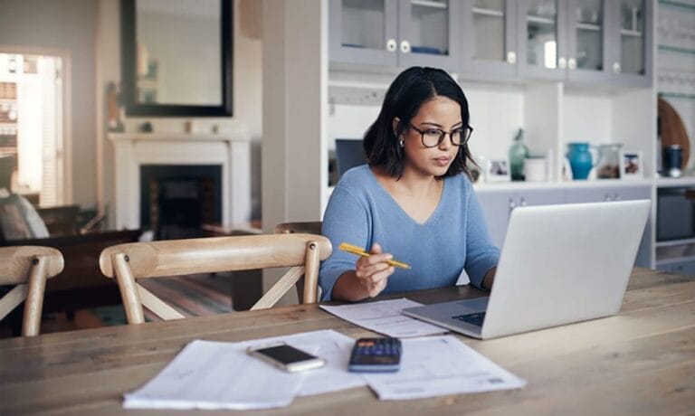 A woman wearing glasses sitting in her living room, working on her laptop.